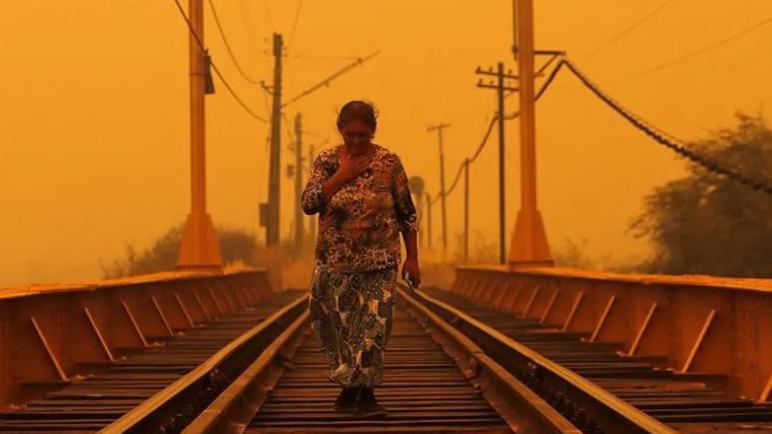 امرأة تمشي على سكة حديد في أجواء تبدو شديدة الحرارة