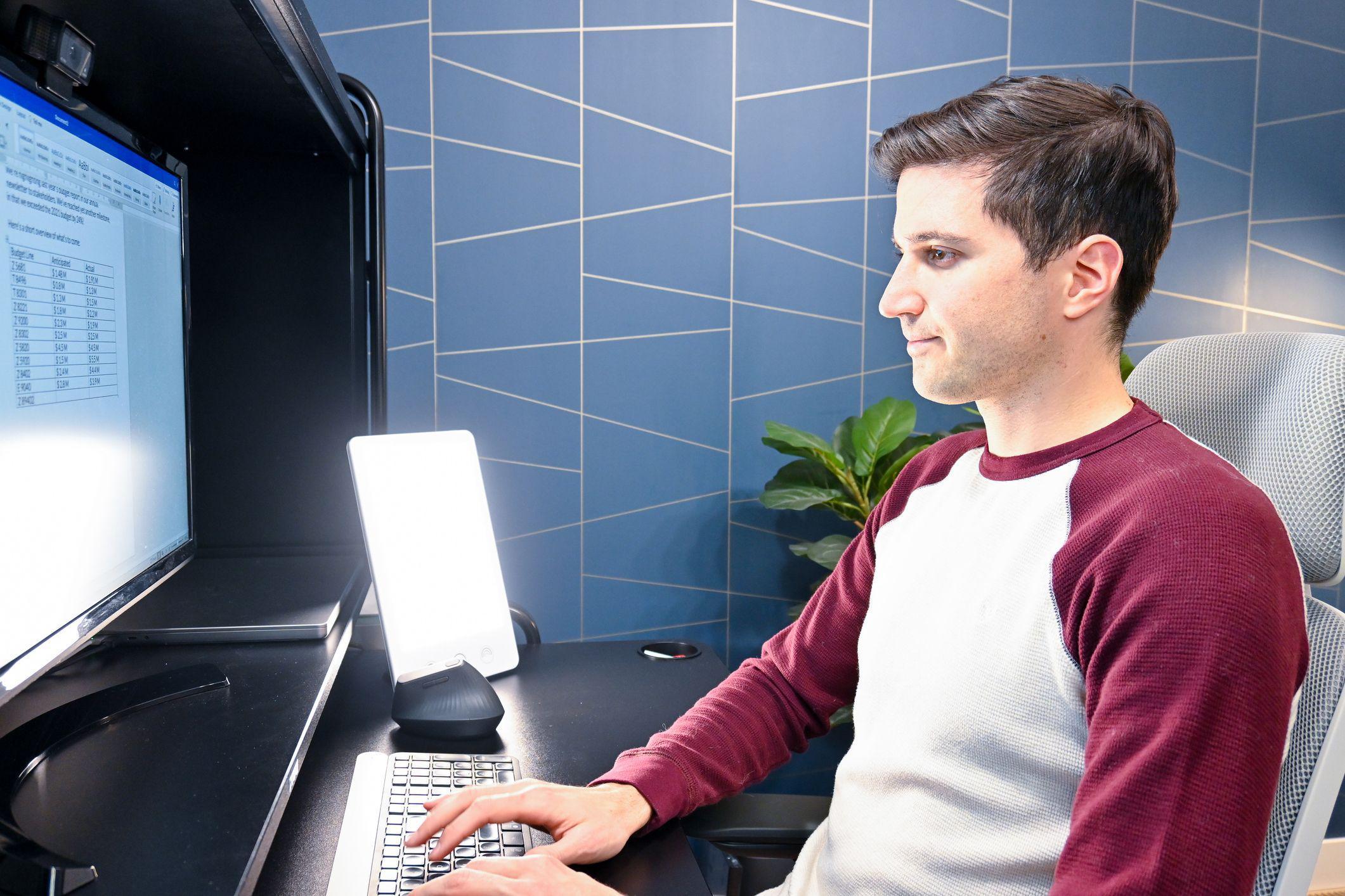 Jovem trabalha no computador com luz terapêutica ao lado