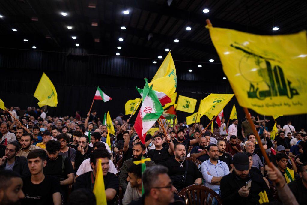 لبنانيون يلوحون بأعلام حزب الله وإيران خلال مشاهدة الأمين العام لحزب الله حسن نصر الله في الضاحية الجنوبية لبيروت في 24 مايو/أيار 2024، بعد مصرع الرئيس الإيراني رئيسي في حادث تحطم مروحية.