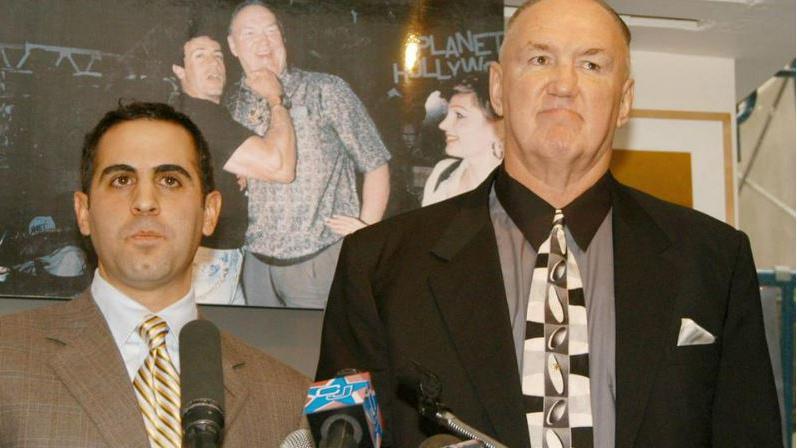 Wepner (kanan) mengumumkan gugatannya terhadap Stallone pada konferensi pers tahun 2003, berpose di depan foto dirinya dengan bintang film tersebut