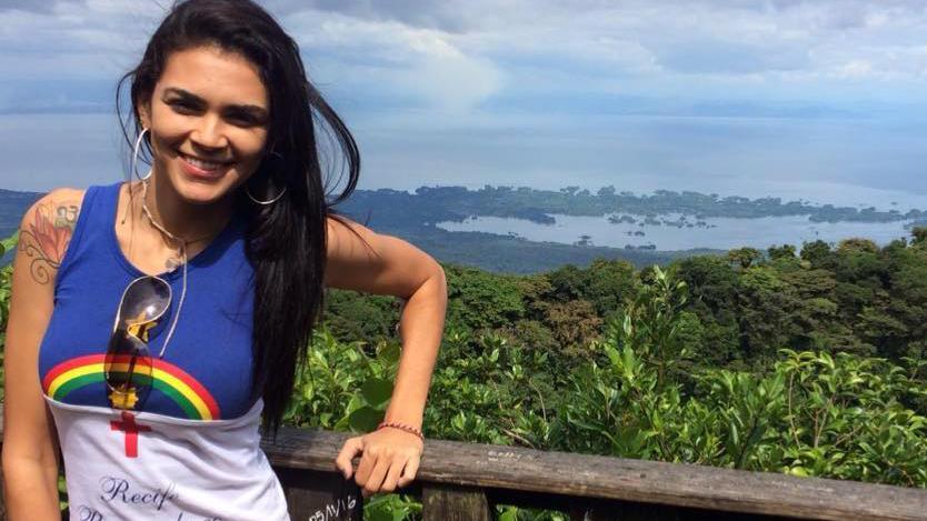 Raynéia sorrindo em frente a paisagem com floresta e água