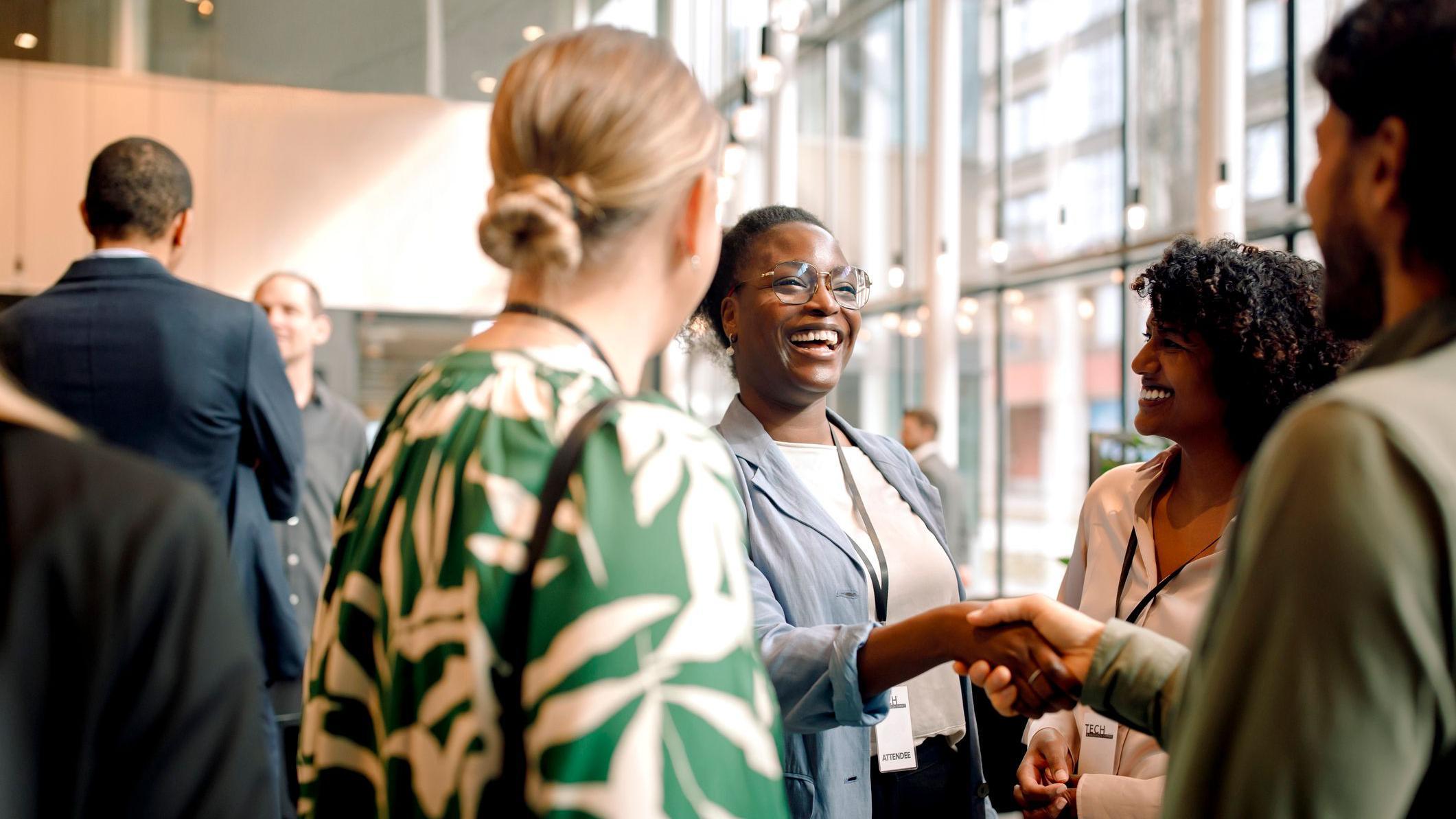 Mulheres e homens com roupas profissionais e crachás de empresa sorrindo e se cumprimentando, em uma roda de conversa