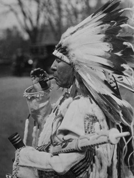أمريكي من السكان الأصليين من قبيلة سيوكس يرتدي الزي التقليدي ويدخن الغليون. صورة من محمية روزبد في ساوث داكوتا تعود إلى عام 1925