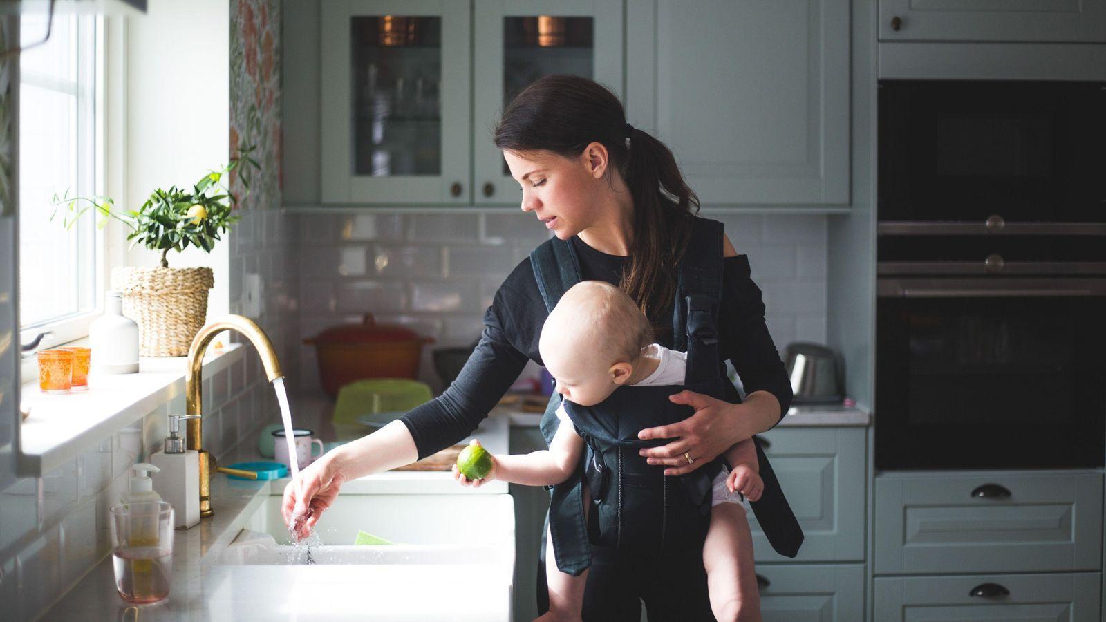 Mãe mexe em pia da cozinha enquanto carrega bebê