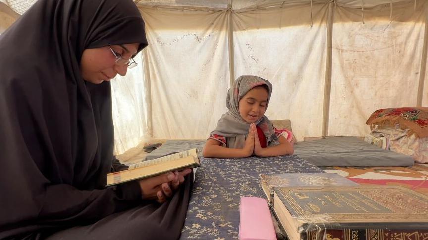 Mujer lee el Corán y su hija reza