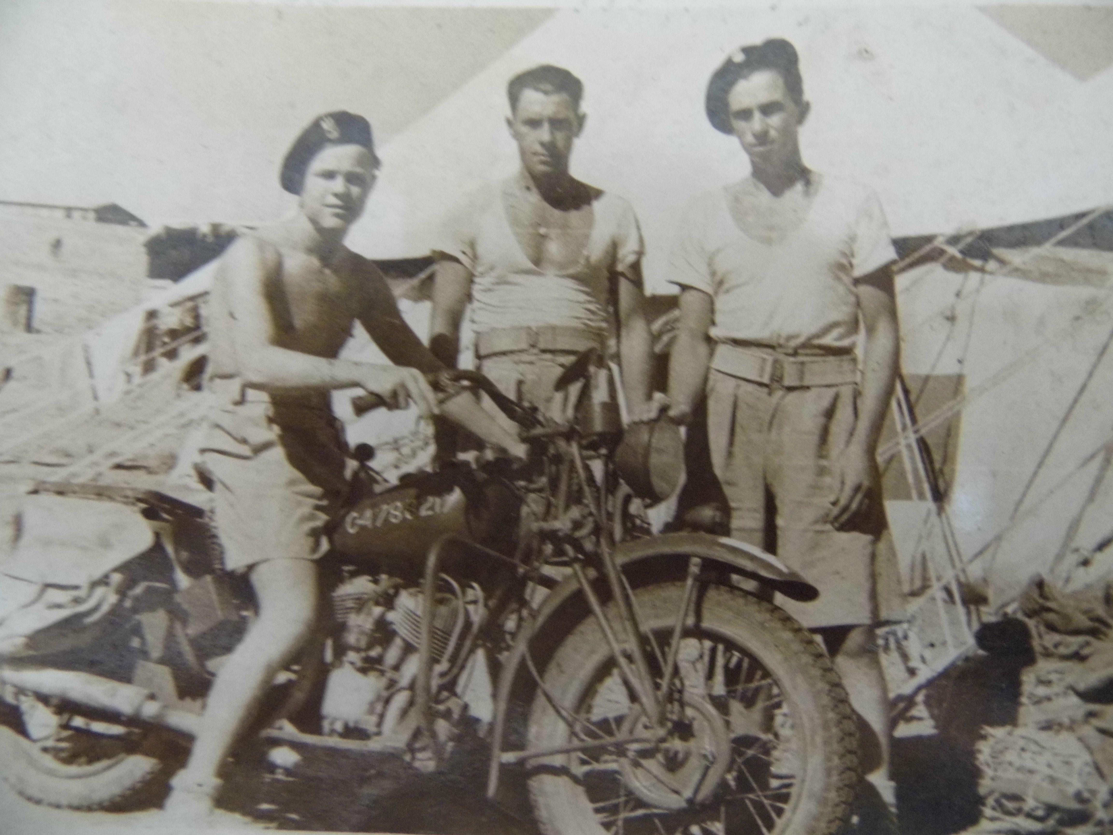 Andrzej Gasior, sem camisa, sentado em sua motocicleta ao lado de outros dois soldados 