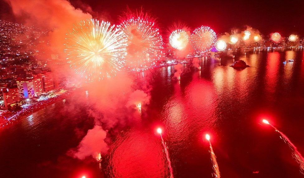 Fuegos artificiales verdes y anaranjados en la playa 