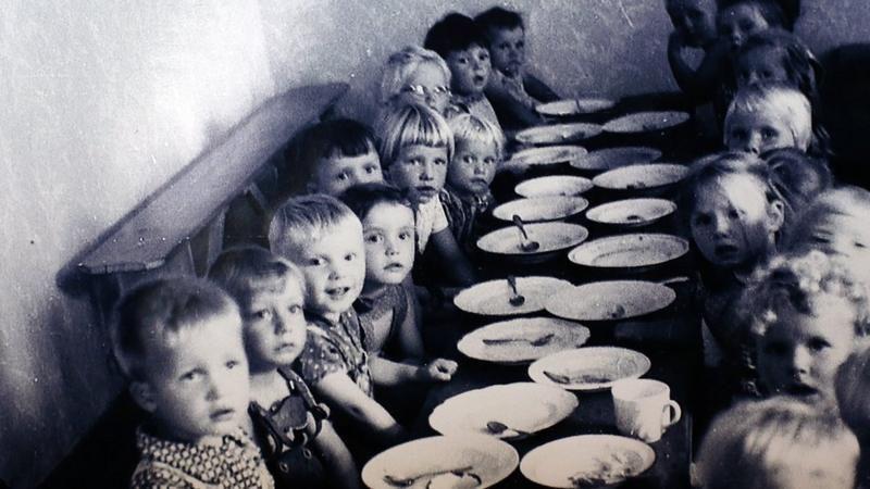 Fotografia em preto e branco de crianças pequenas brancas em frente a uma mesa