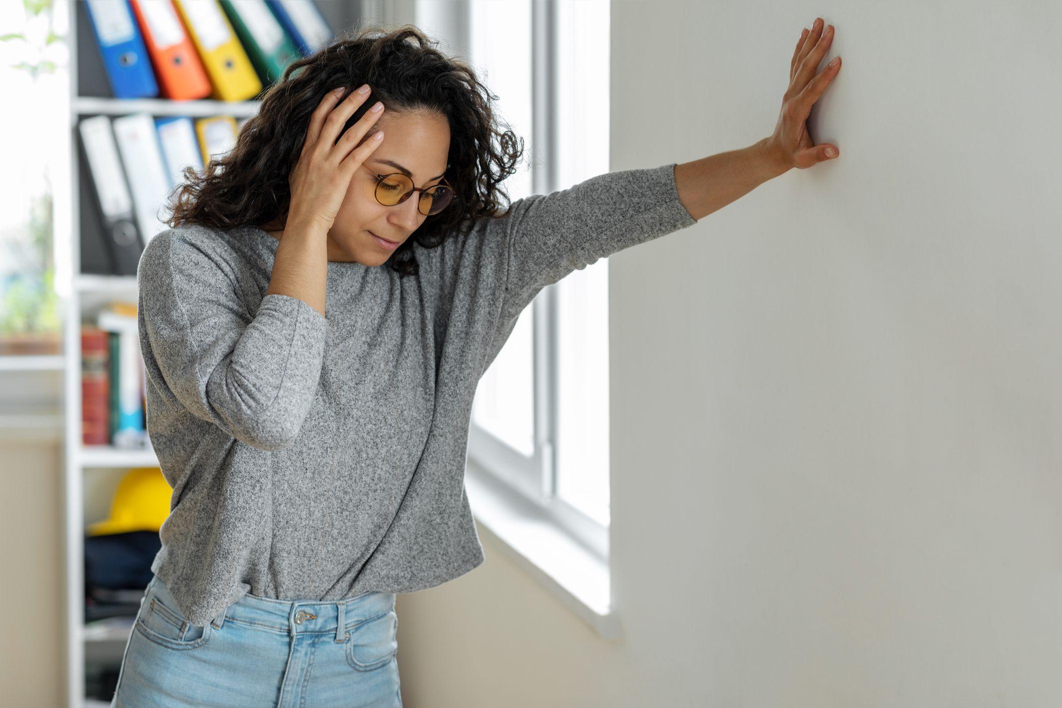 A woman leans against a wall and holds her head