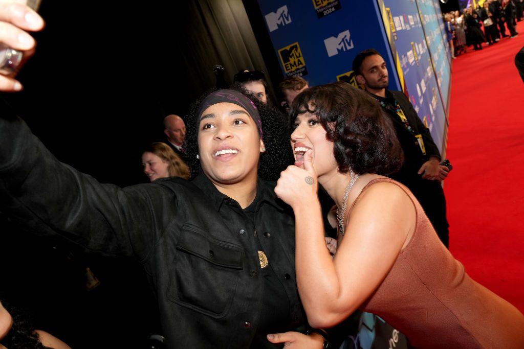 Raye gives a thumbs up while posing for a selfie with a fan on the red carpet