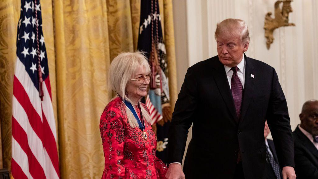 Miriam Adelson e Donald Trump lado a lado em sala, em frente a bandeira dos EUA