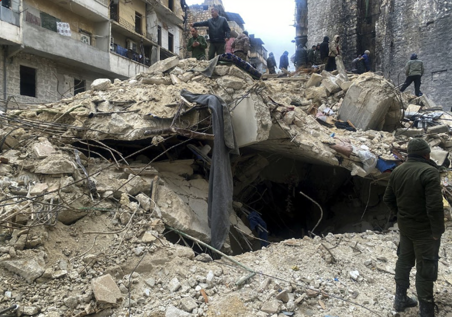 A collapsed building with people standing on the rubble