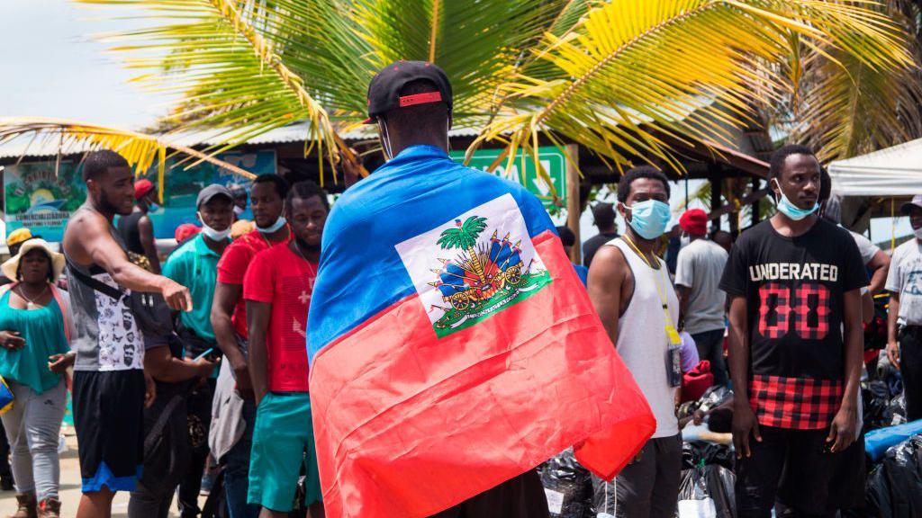 Un migrante haitiano con la bandera nacional de Haití mientras miles de migrantes haitianos, africanos y cubanos tratan de pasar hacia la frontera Colombia - Panamá en barco para luego seguir a los Estados Unidos.