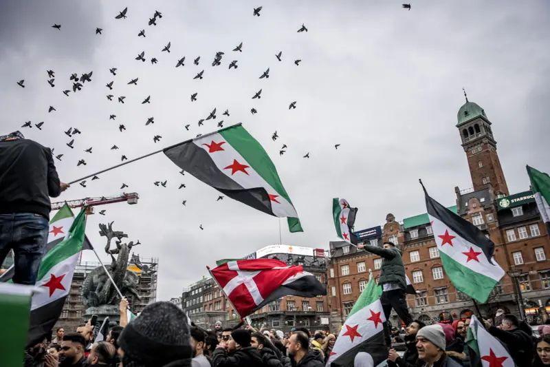 La gente ondea banderas sirias y danesas en una plaza de Copenhague, Dinamarca.