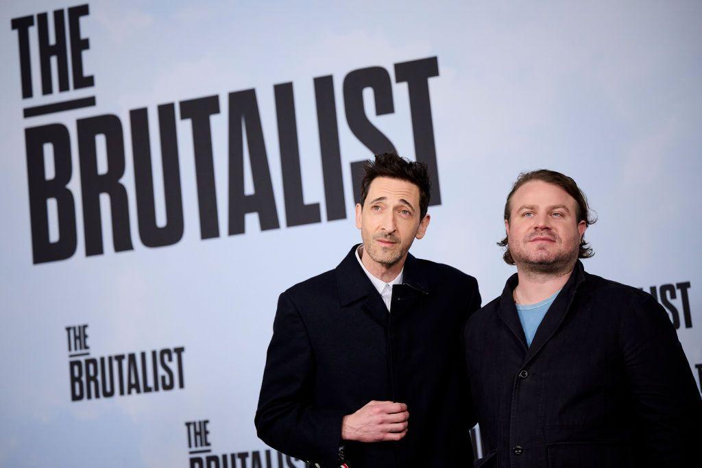 Adrien Brody y Brady Corbet con un cartel detrás con la promoción de The Brutalist