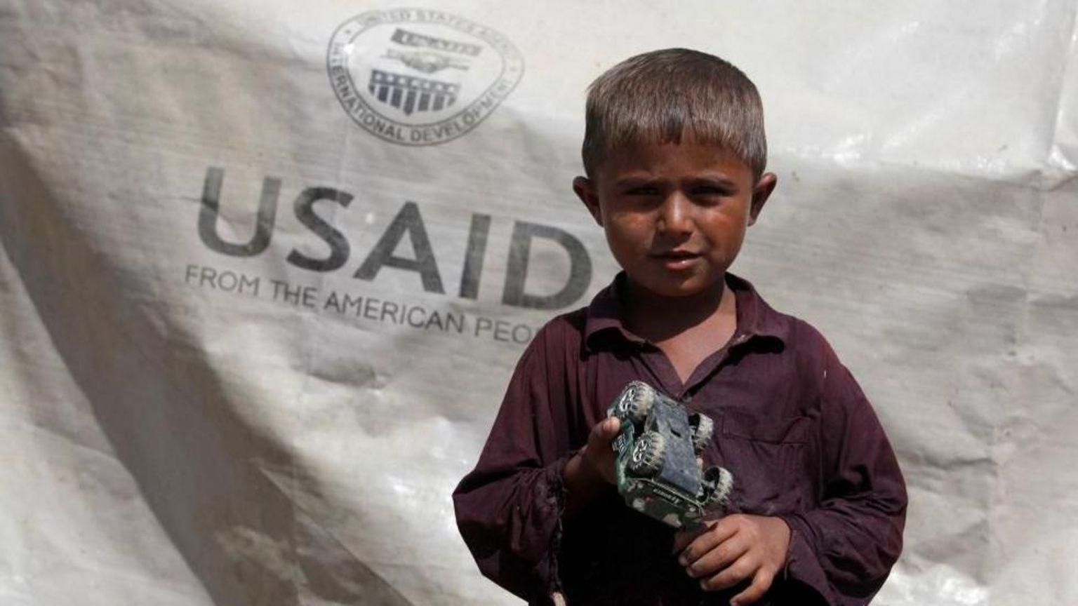 Un niño con un juguete y una lona con el lema de USAID.