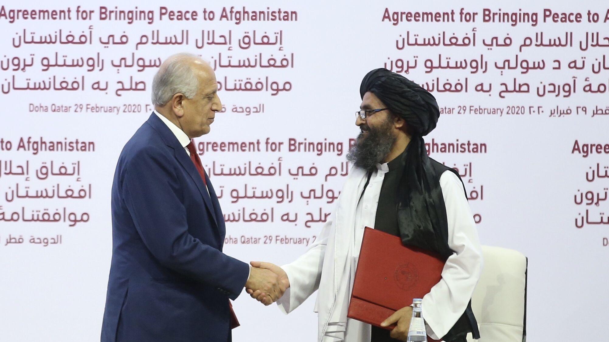 Perwakilan Khusus AS untuk Rekonsiliasi Afghanistan, Zalmay Khalilzad (kiri), dan salah satu pendiri Taliban, Mullah Abdul Ghani Baradar (kanan), berjabat tangan setelah menandatangani perjanjian damai antara AS dan Taliban di Doha, Qatar, pada 29 Februari 2020.