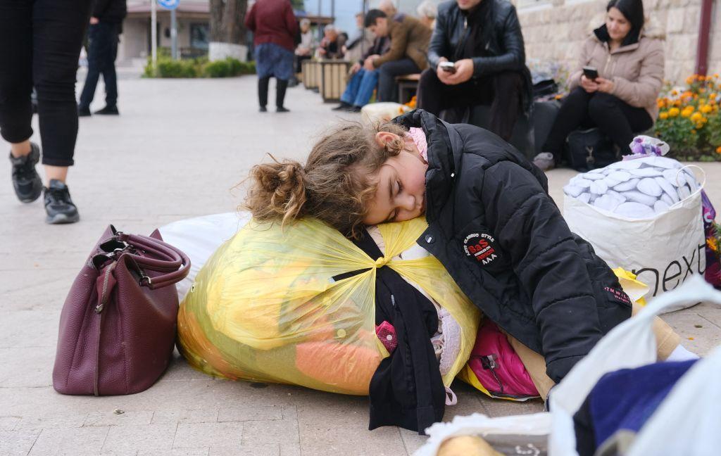 Una niña duerme en el piso apoyada sobre una bolsa con ropa.