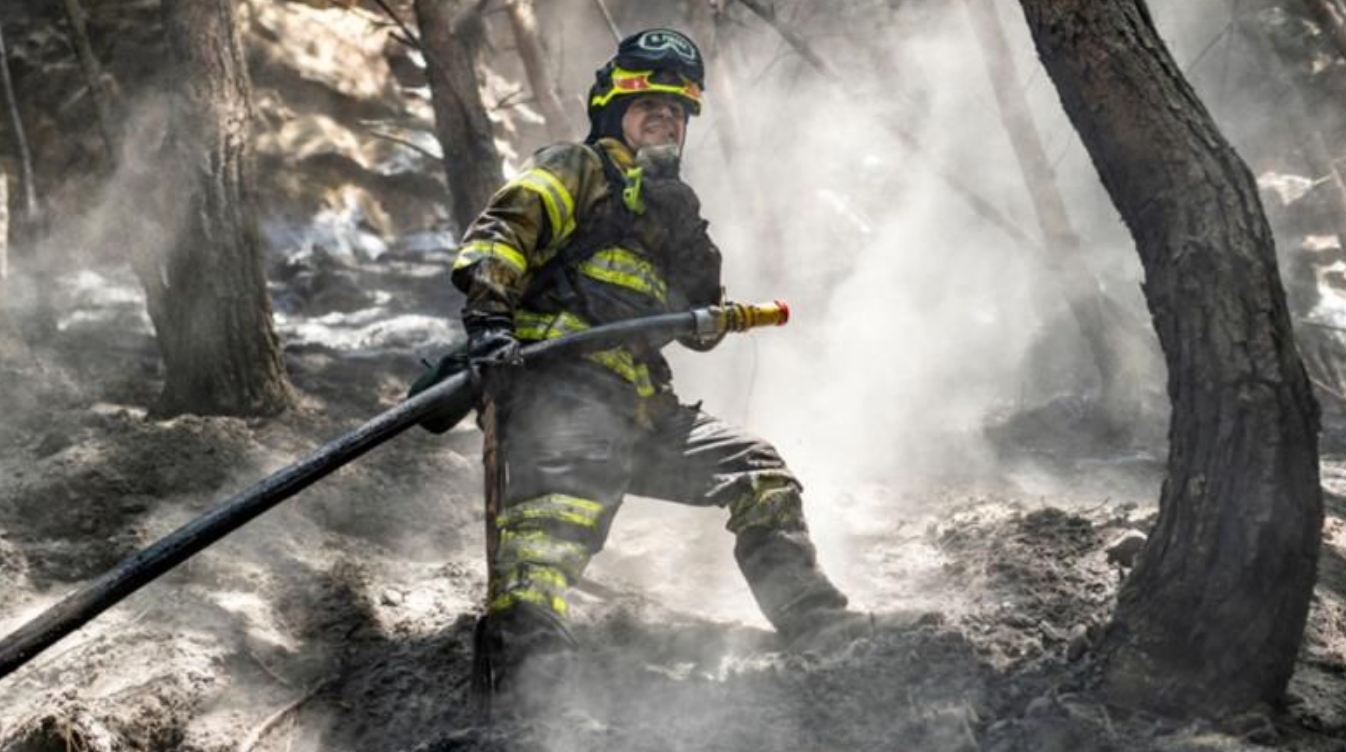 Imagem de um bombeiro combatendo incêndios florestais em um cenário devastado por fumaça e chamas, simbolizando os efeitos das mudanças climáticas observadas em 2024, como secas e calor intenso.