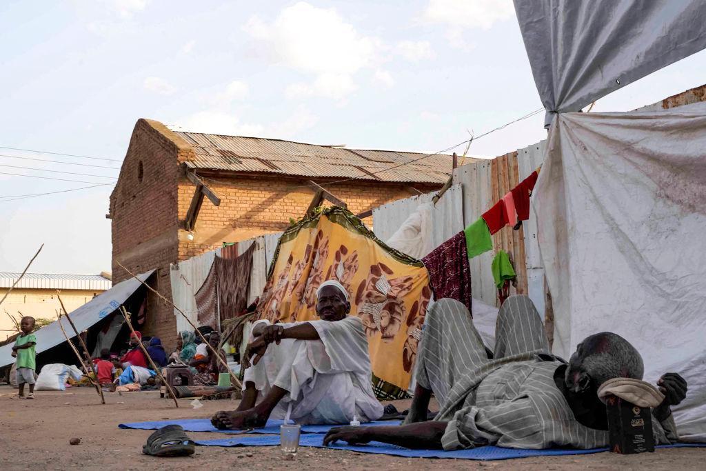 Homens sentam e deitam do lado de fora de tendas e abrigos montados na escola secundária de Hasahisa em 10 de julho de 2023, que foi transformada em um acampamento improvisado para abrigar os deslocados internos