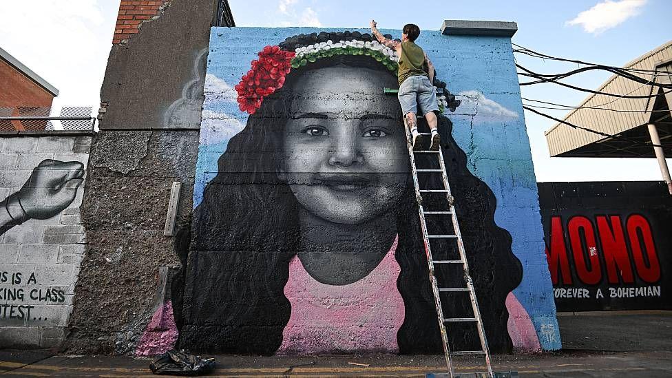 Un artista en Dublin subido a una escalera pinta un mural con el rostro de Hind Rajab