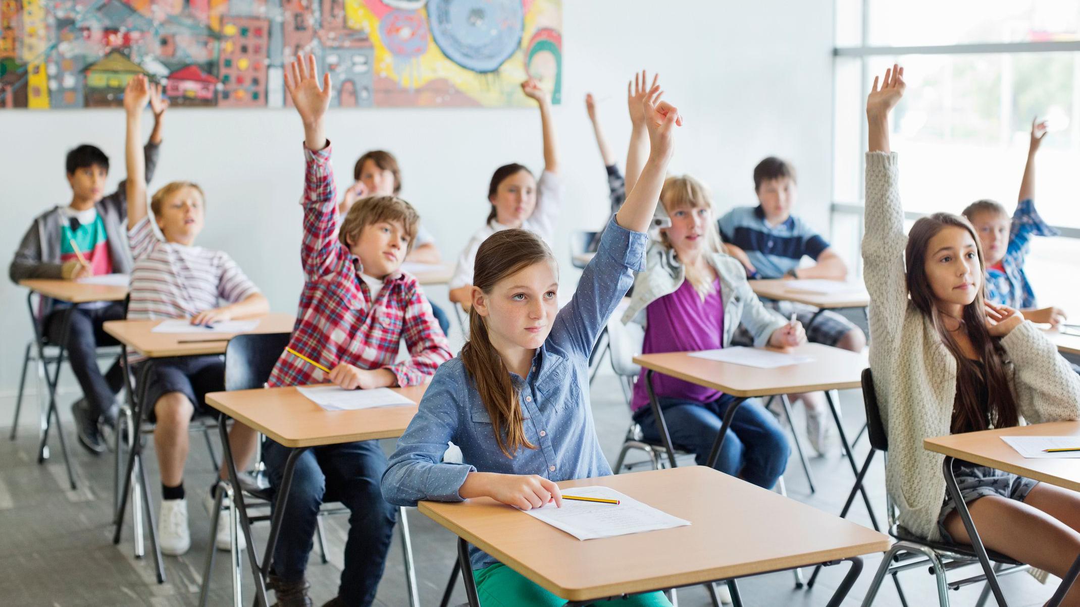 Estudiantes con las manos levantadas en el aula