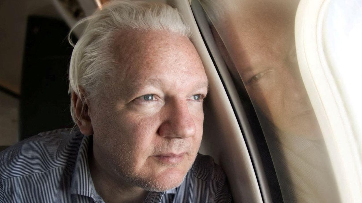 Julian Assange mira por la ventana del avión en el que abandonó Reino Unido