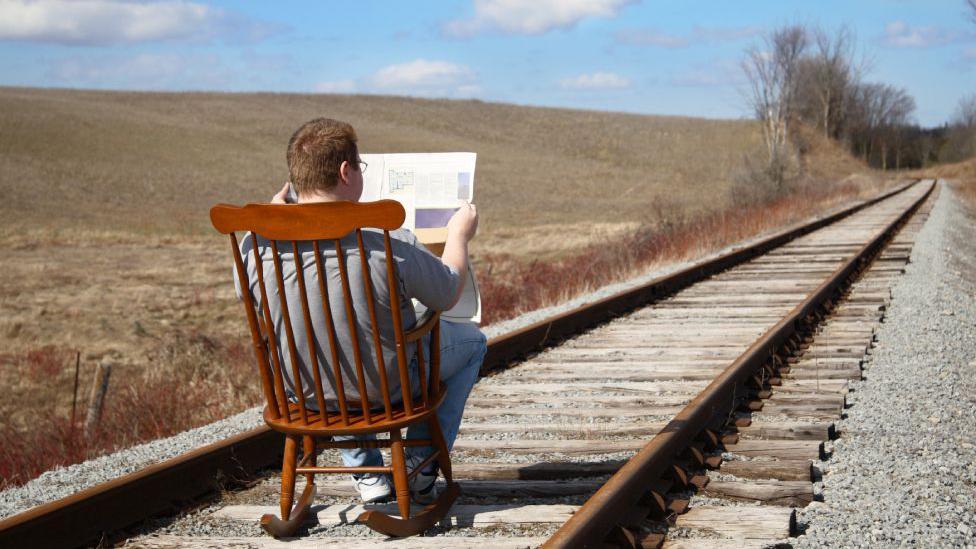 Hombre sentado leyendo el periódico en una ferrovía