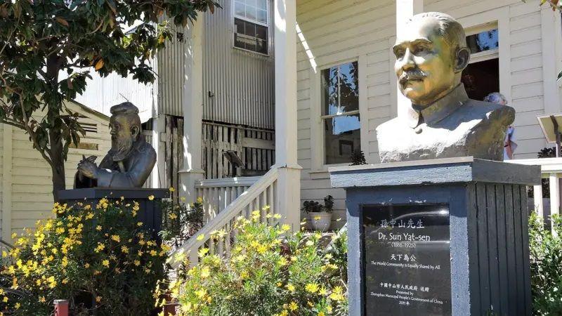 Imagem da frente de uma casa, com dois bustos de bronze, um de cada lado da escada. No da direita, está escrito 'Dr. Sun Yat-sen' 