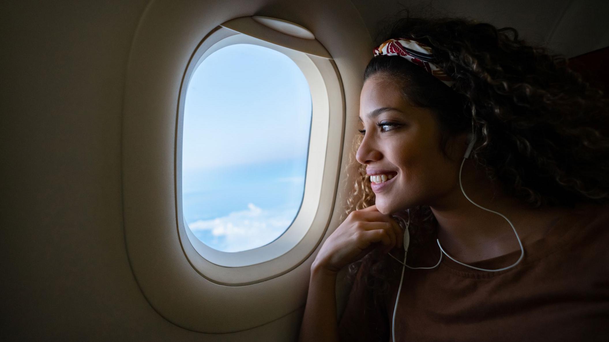 Mujer en un avión mirando por la ventanilla de su asiento. 