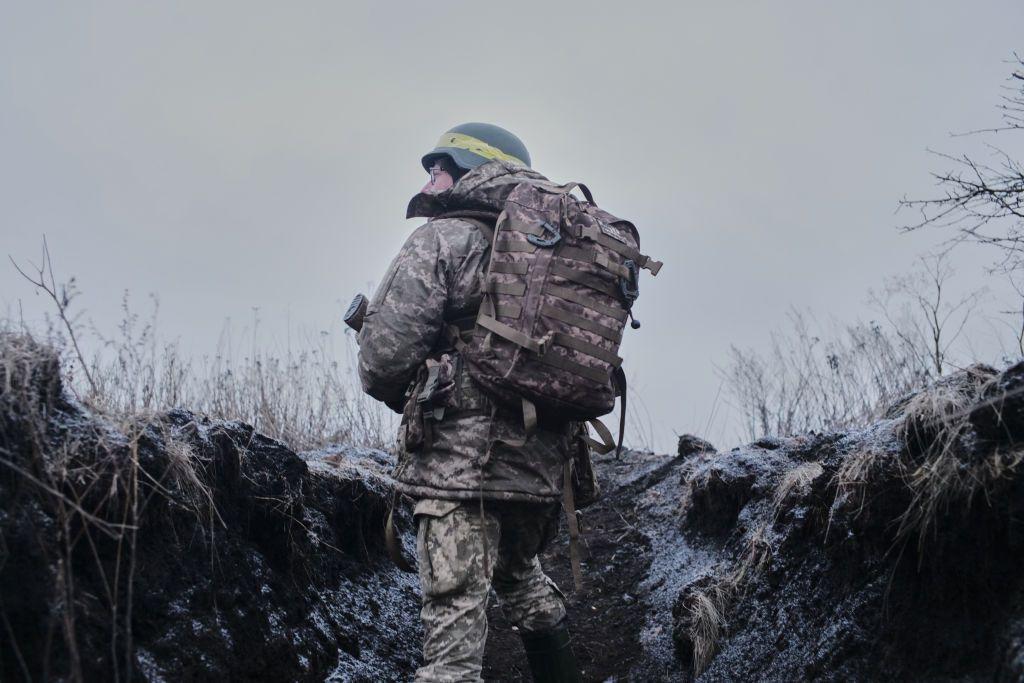 Soldado ucraniano fotografado de costas,  com armamento, mochila e capacete.