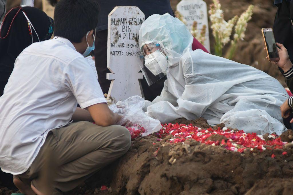 Seorang anggota keluarga yang mengenakan masker wajah berduka selama pemakaman seorang kerabatnya di pekuburan Rorotan, Jakarta Timur, 8 Agustus 2021.