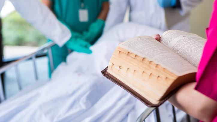 Mulher com Bíblia na frente de cama do hospital