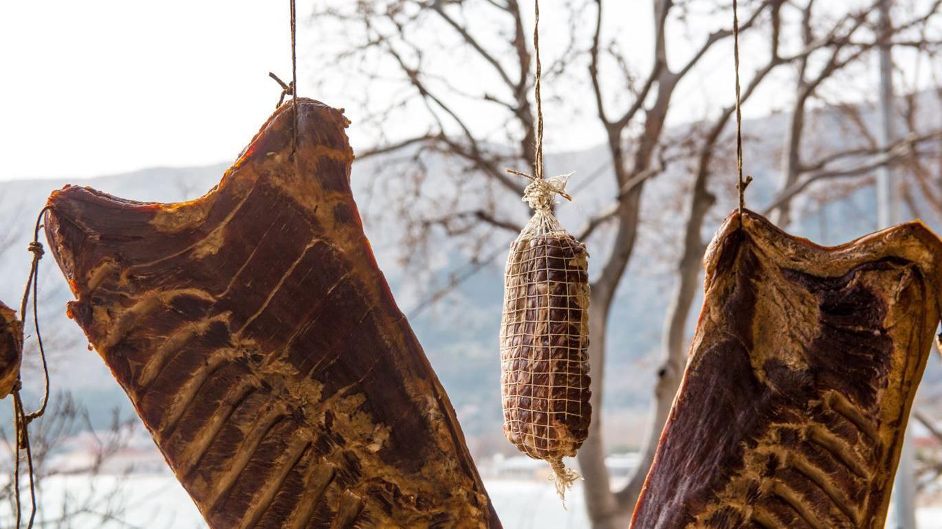 Três grandes pedaços de carne pendurados para secar ao ar