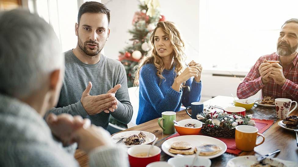 Hombre discutiendo con otras personas en torno a una mesa durante la Navidad