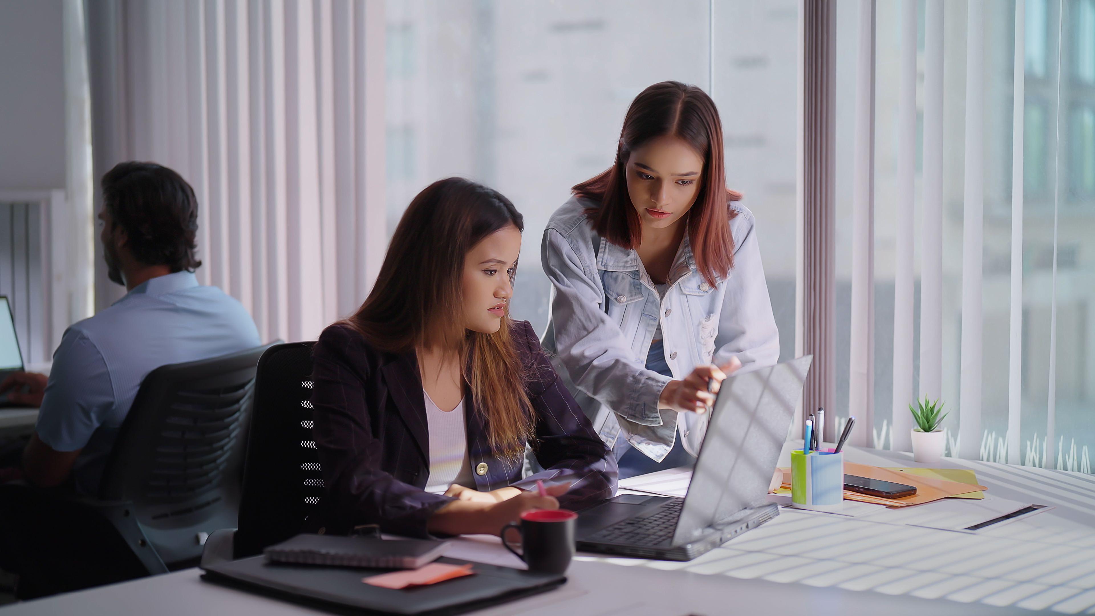 dos mujeres conversan en una oficina frente a un computador 