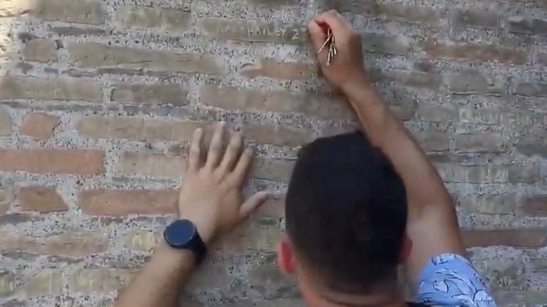 Tourist carving his name and that of his girlfriend on the wall of the Roman Colosseum