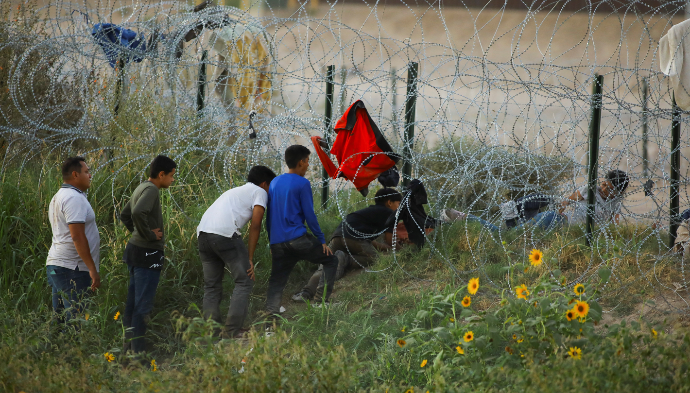 Varias personas cruzan una alambrada en la frontera de EE.UU.