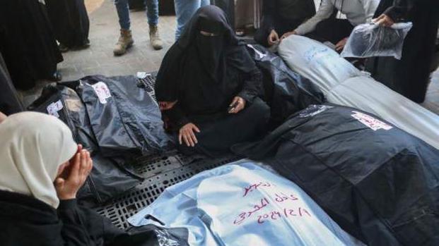 فلسطينيون يجلسون وسط جثث ضحايا الهجوم الإسرائيلي
