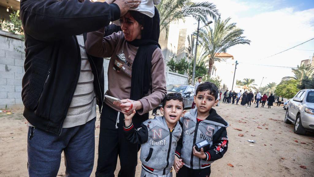 Una mujer herida junto a dos niños en Gaza.