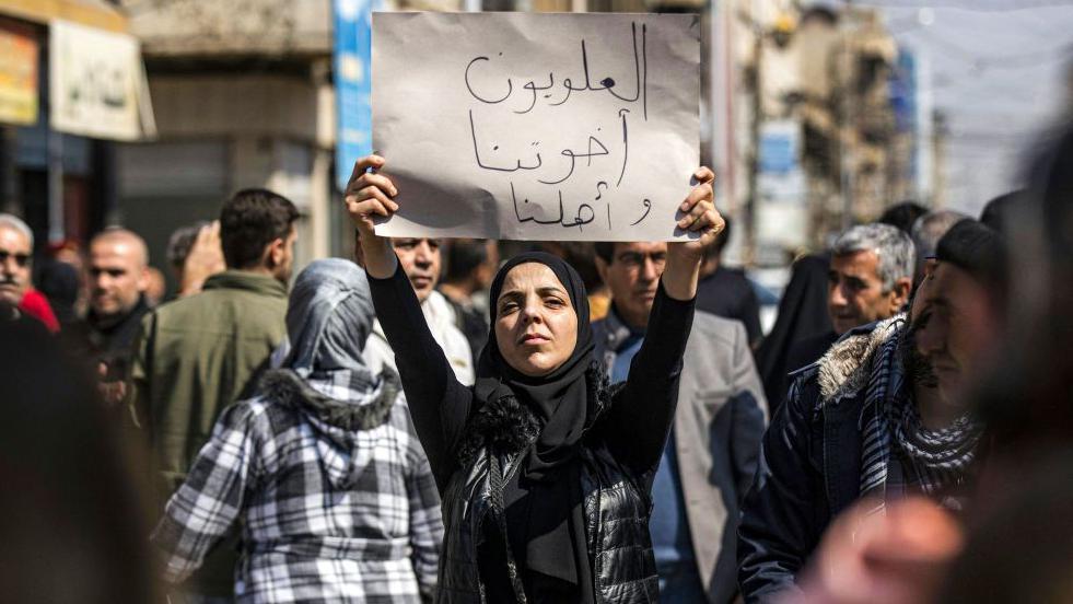 Una mujer sostiene un cartel que dice en árabe "Los alauitas son nuestros hermanos y familia" durante una manifestación multitudinaria en la ciudad de Qamishli, en el noreste de Siria.
