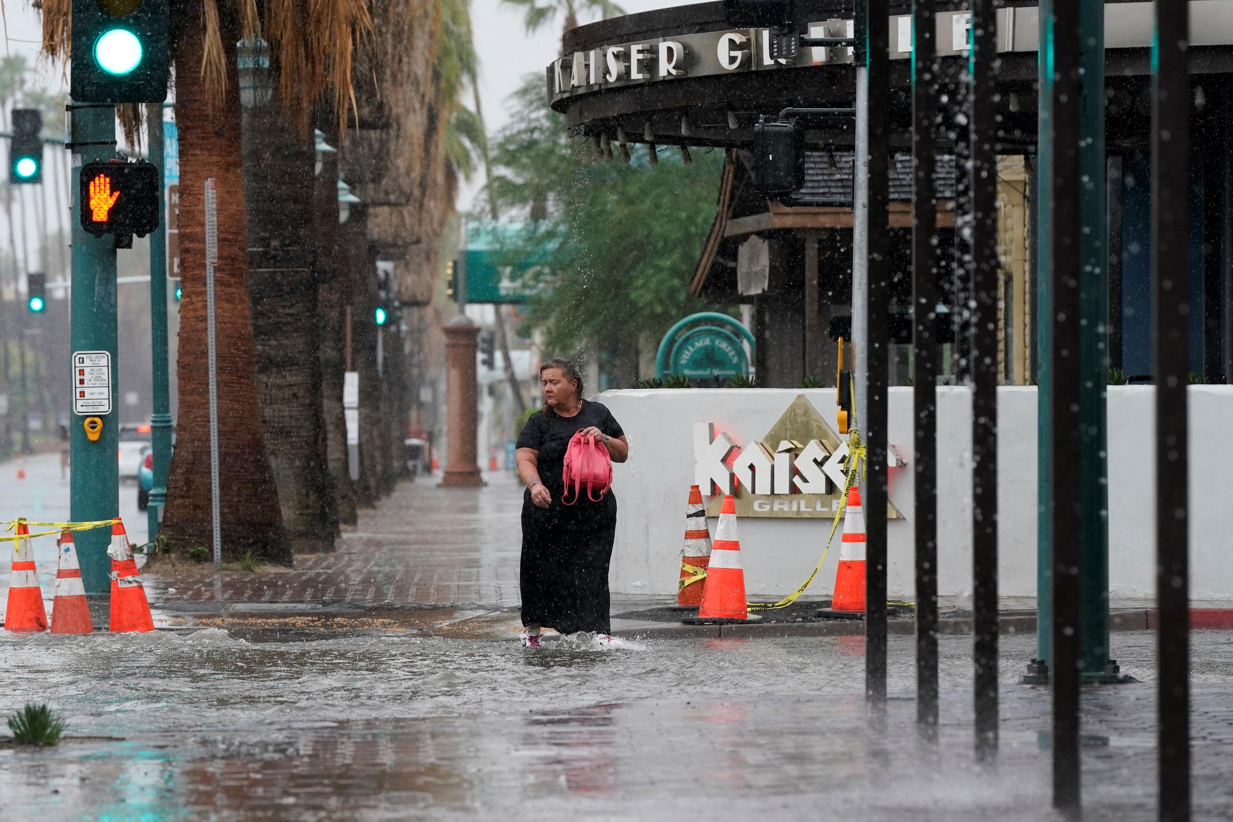 Una mujer camina sobre el agua estancada durante la tormenta tropical Hilary en Palm Springs, California.