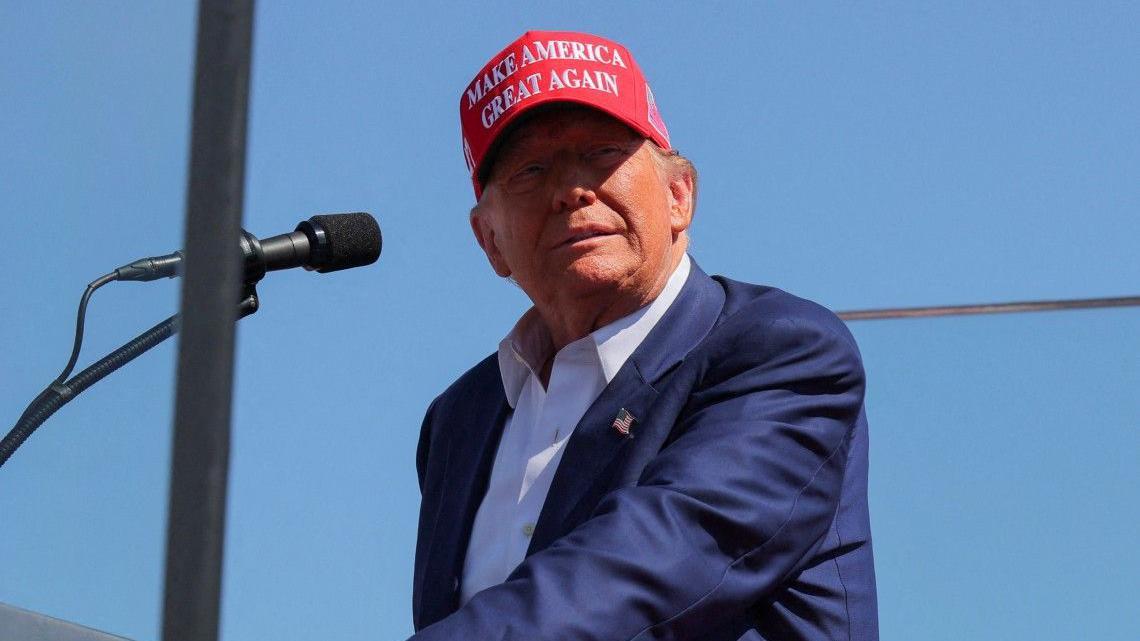 Donald Trump con una gorra roja que dice: Make America Great Again en un evento al aire libre