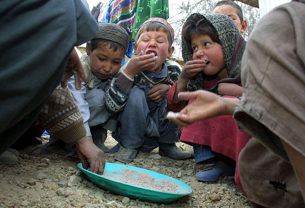 Niños afganos en un campo de refugiados comiendo de un plato.