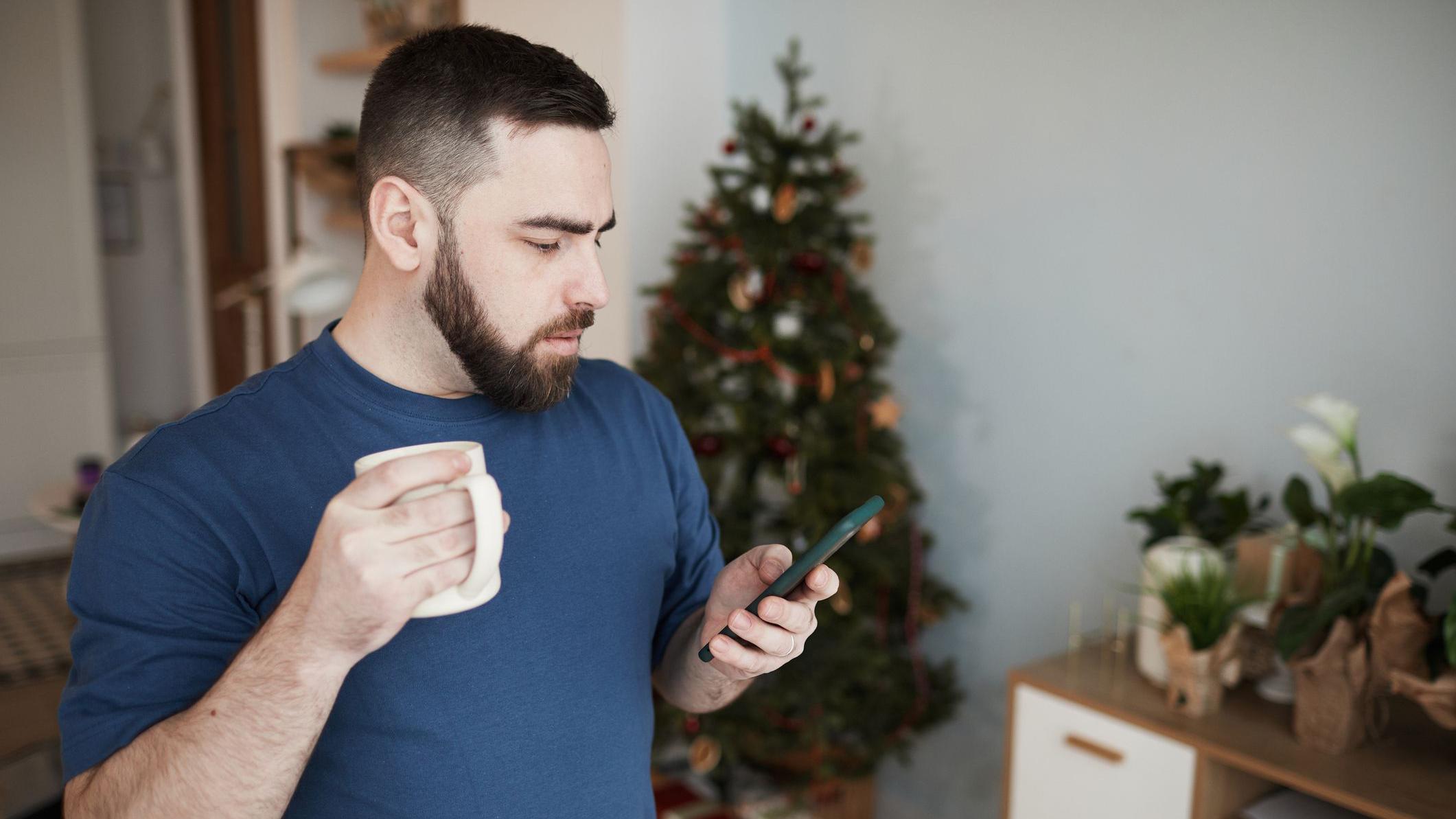 Homem usando o celular com árvore de Natal ao fundo