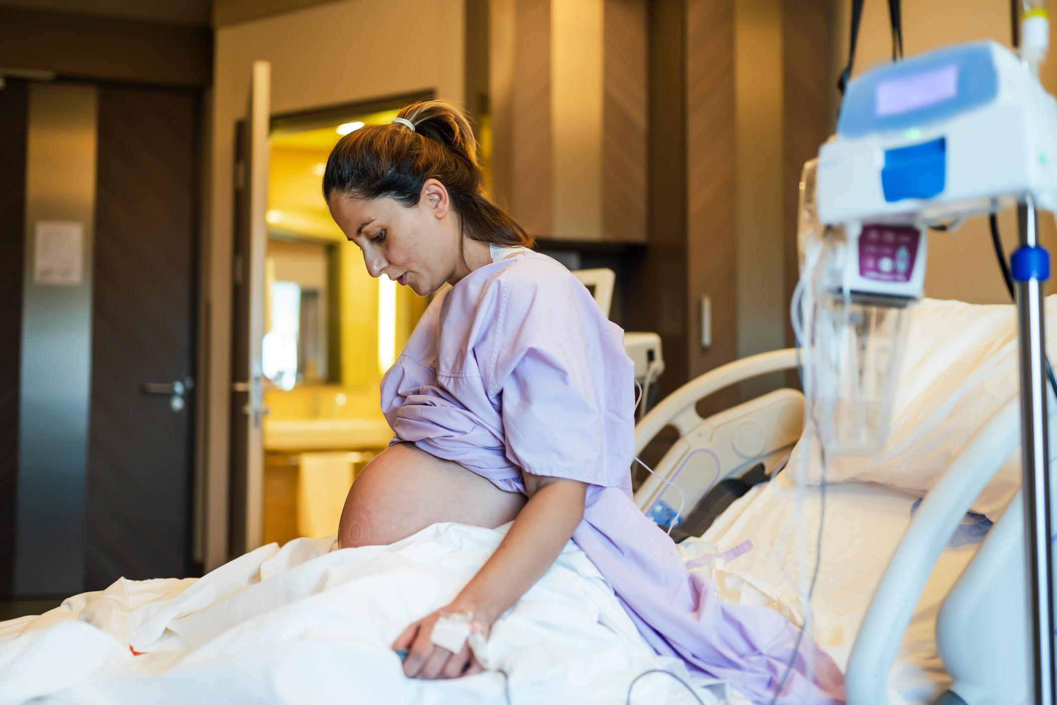 Mulher grávida sentada em cama de hospital prestes a dar a luz