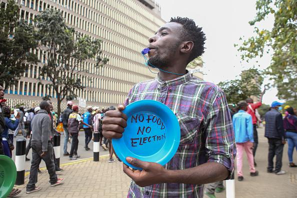 Homem queniano durante protesto contra a inflação, com um apito na boca e segurando um prato vazio onde se lê: 'Sem comida, sem eleição'