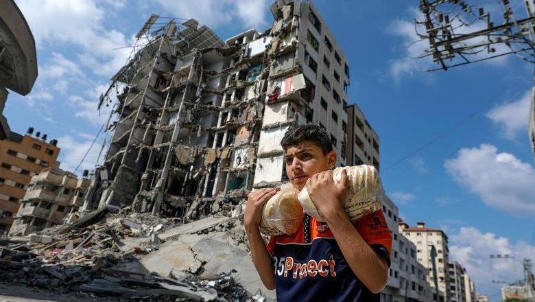 شاب فلسطيني يحمل كيسا من الخبز ويسير بالقرب من المباني التي دمرتها الغارات الإسرائيلية الأخيرة في حي الرمال بمدينة غزة