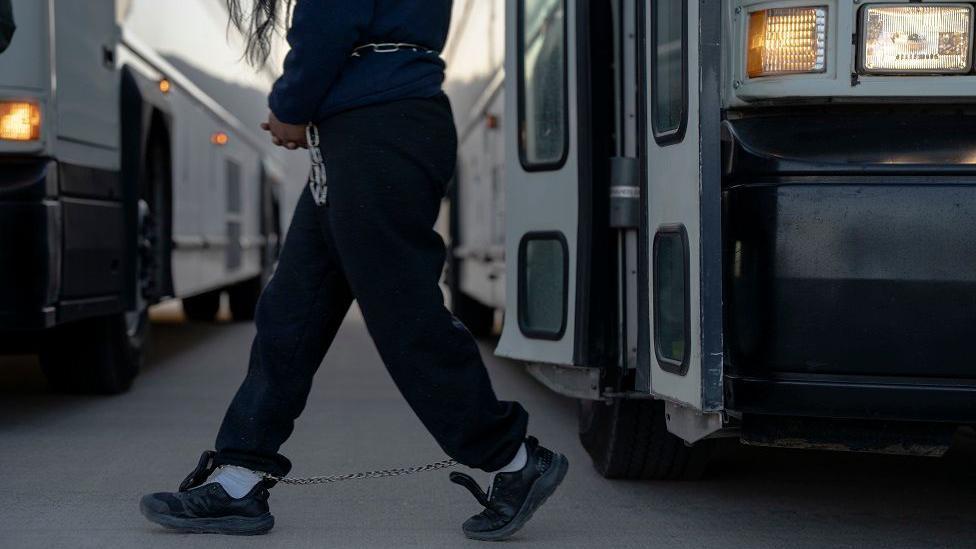 Una inmigrante indocumentada con una cadena en los pies y en la cintura caminando