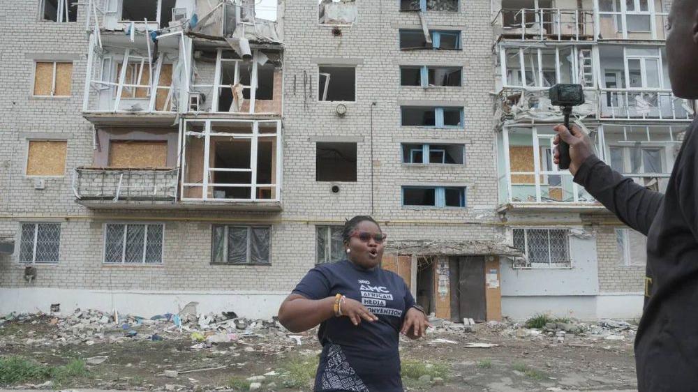 Ivy Setordjie em frente a um prédio destruído.